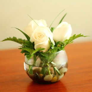 Centro de mesa en forma de pecera con rosas blancas y helecho.