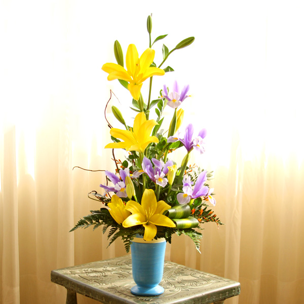 Florero de color celeste con Liliums amarillos y flores lilas.