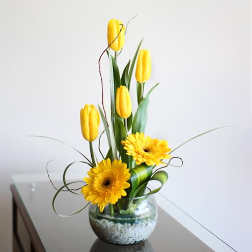 Pecera con tulipanes y gerberas amarillas.