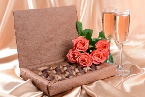 Delicious chocolates in box with flowers on gold background
