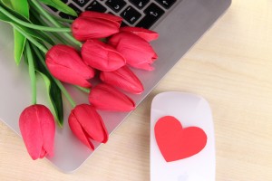 Computer with red heart and flowers on table close up