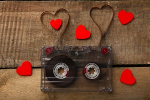 Audio cassette with magnetic tape in shape of hearts on wooden background