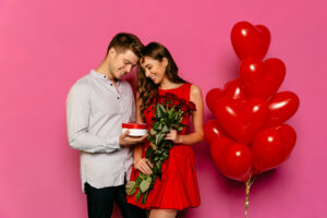 Pareja en sesión de fotos con regalo, rosas rojas y globos de corazón.