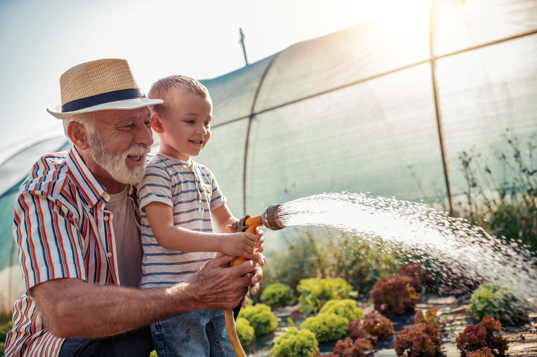Abuelo y nieto regando un jardin.