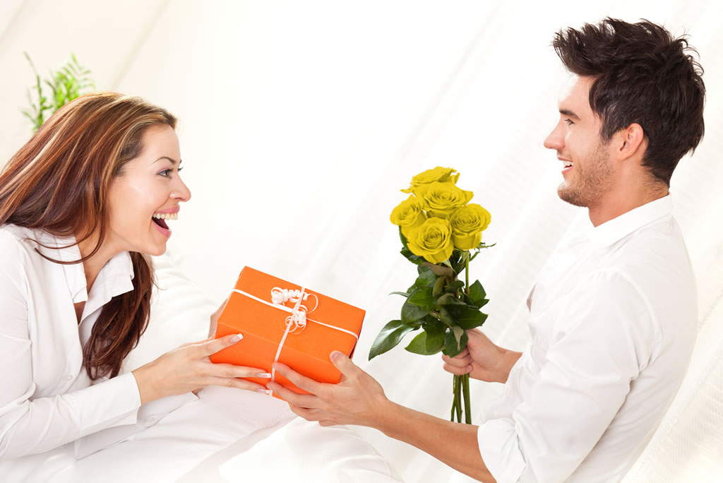 Mujer regalando un presente y rosas amarillas a hombre.
