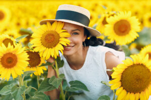 Mujer bonita con sombrero y vestido blanco, feliz por estar en un campo de girasoles.